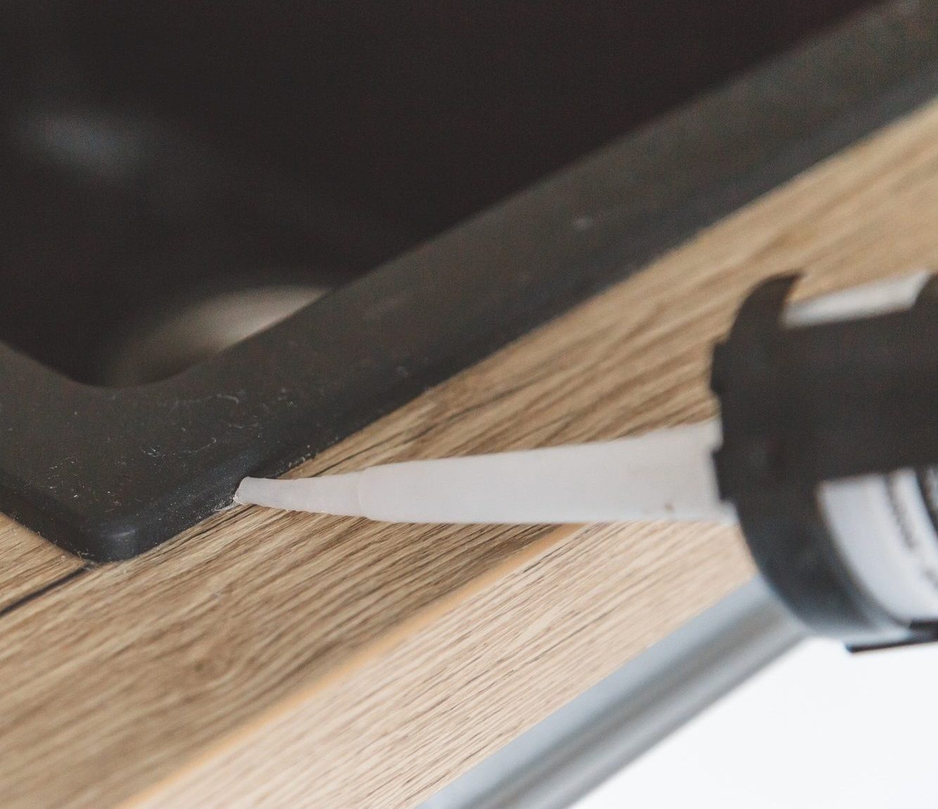 Man sealing kitchen sink joint between sink and countertop by silicone sealant